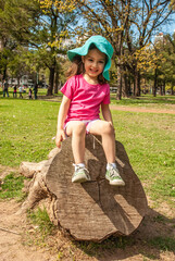 Cheerful little girl sitting on a tree in the park