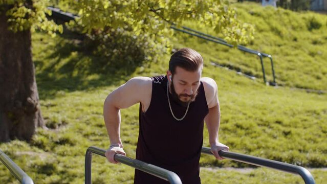 Athletic lebanese man in sportswear practicing dips on parallel bars, training triceps. Young middle eastern guy on playground. Sports health fitness routine, workout. Strength motivation. Outdoor gym