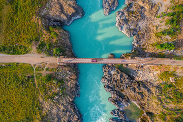 Red car on suspension Oroktoysky bridge over Katun river in valley of Altai Mountains, aerial top view. Travel landmark in Chemal Siberia, Russia
