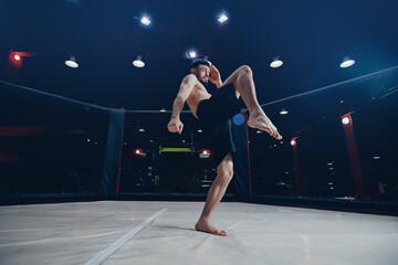 MMA Training of fighter without rules in octagon cage kick in flight on dark background