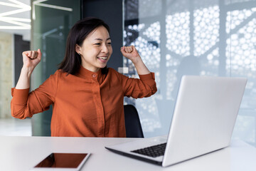 Fototapeta na wymiar Successful asian businesswoman working inside office with laptop, female employee received online message victory and good achievement results, female partner holding hands up celebrating triumph.