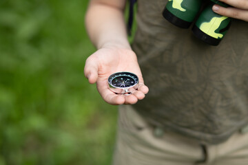 Caucasian cute kid boy with a backpack travels with a compass. Child boy scout holding in a hand compass in the forest during a hike. Children summer outdoor activity.