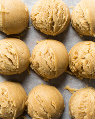 Scoops of vanilla cookie dough on a parchment lined cookie sheet, plain vanilla cookie dough about to be baked