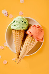 Various colorful ice cream scoops or balls with waffle cones on yellow background. Top view