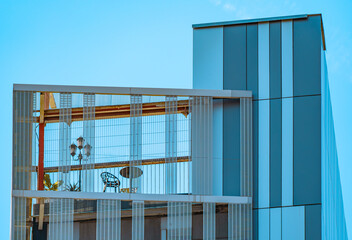 Detail of the facade and structure of a modern, avant-garde and minimalist building covered with large rectangular blue crystals and a terrace in the attic with a lamppost, small table vintage chair