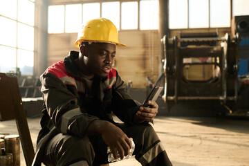 Young African American engineer looking at smartphone screen and communicating in video chat while...