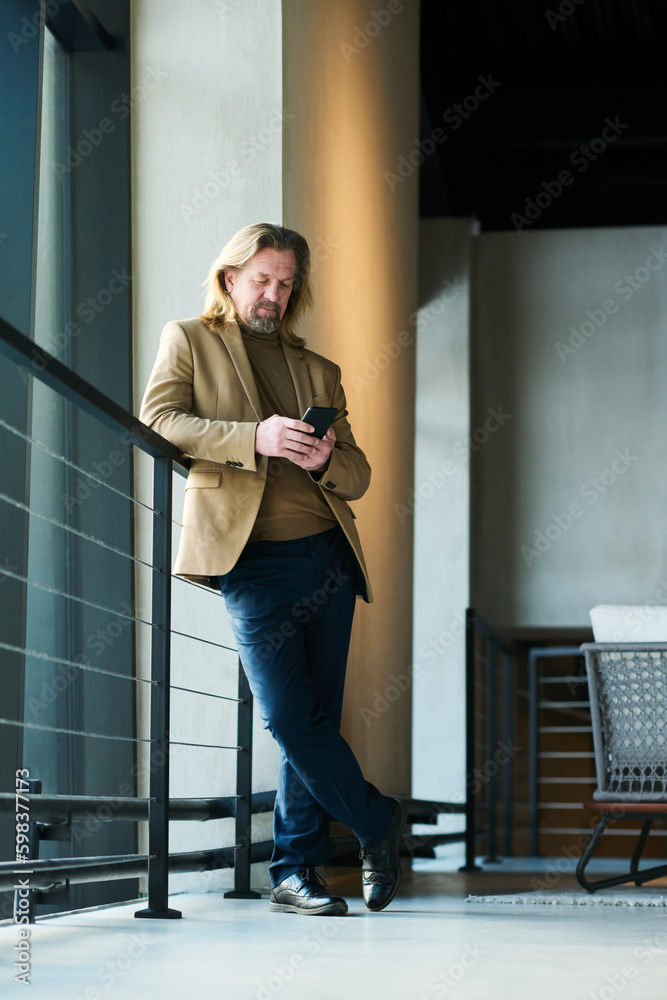 Aufkleber mature elegant male entrepreneur in smart casualwear using smartphone while standing by railings and