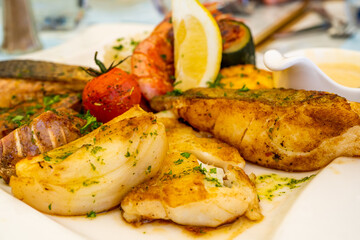 Grilled delicious fish fillets and shrimps with vegetables and lemon slices. Mediterranean diet.