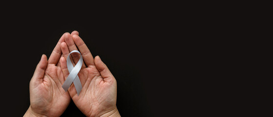 World Brain Tumor day. Person's hands are holding a gray ribbon on black background. This is...