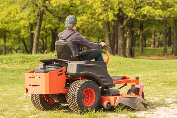 A young teenage boy is riding a zero turn lawn mower and using it to mow. - obrazy, fototapety, plakaty