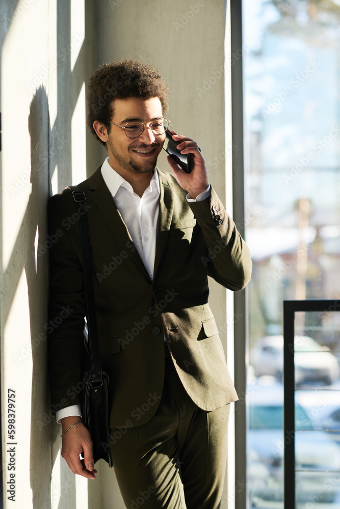 Aufkleber young smiling multi-ethnic white collar worker with handbag on shoulders talking on smartphone while