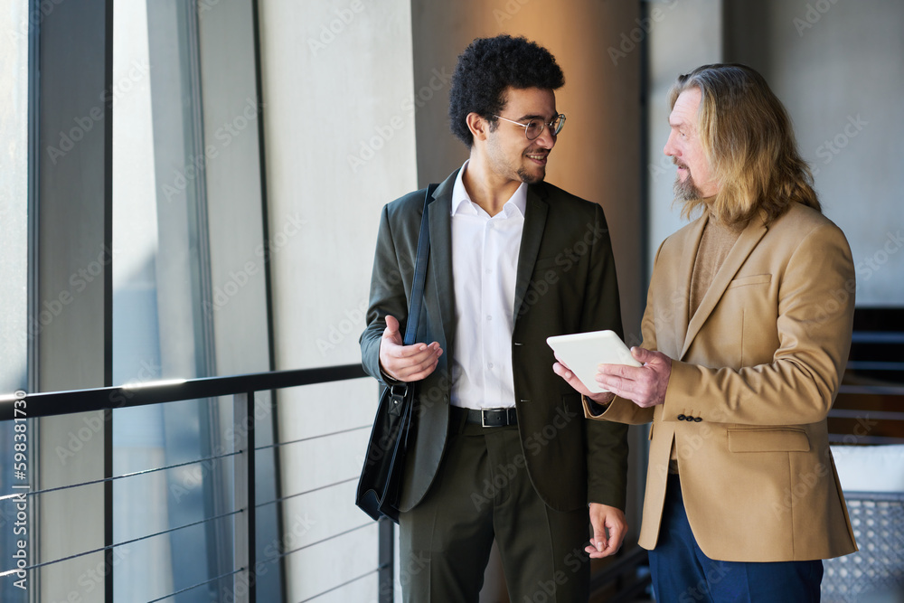 Leinwandbilder young smiling businessman explaining something to mature colleague with tablet during presentation o