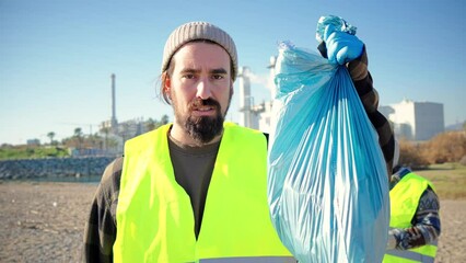 Angry volunteer ecologist looking at all the plastic garbage he has collected from the beach. serious environmental activist holding up a trash bag showing his disagreement with the dirt Generative AI