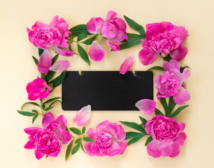 Garland of beautiful pink peonies on yellow paper background with wooden desk for congratulations or invitations. Creative floral wreath.  Greeting card for  holiday.