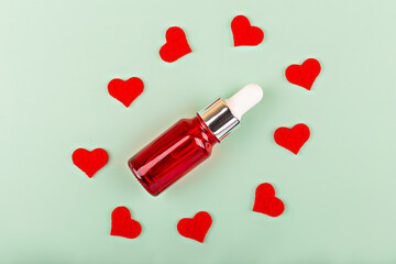 Red cosmetic bottle with dropper in circle of small red hearts on light green background. The concept of care, love, body care