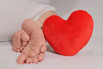 Clean and soft female feet, girl is sitting with her legs folded, next to red heart. Valentines...