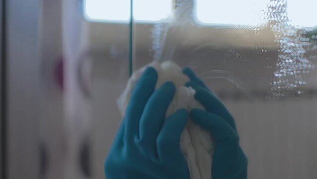 Close up women hands with blue gloves cleaning a mirror surface using spray liquid