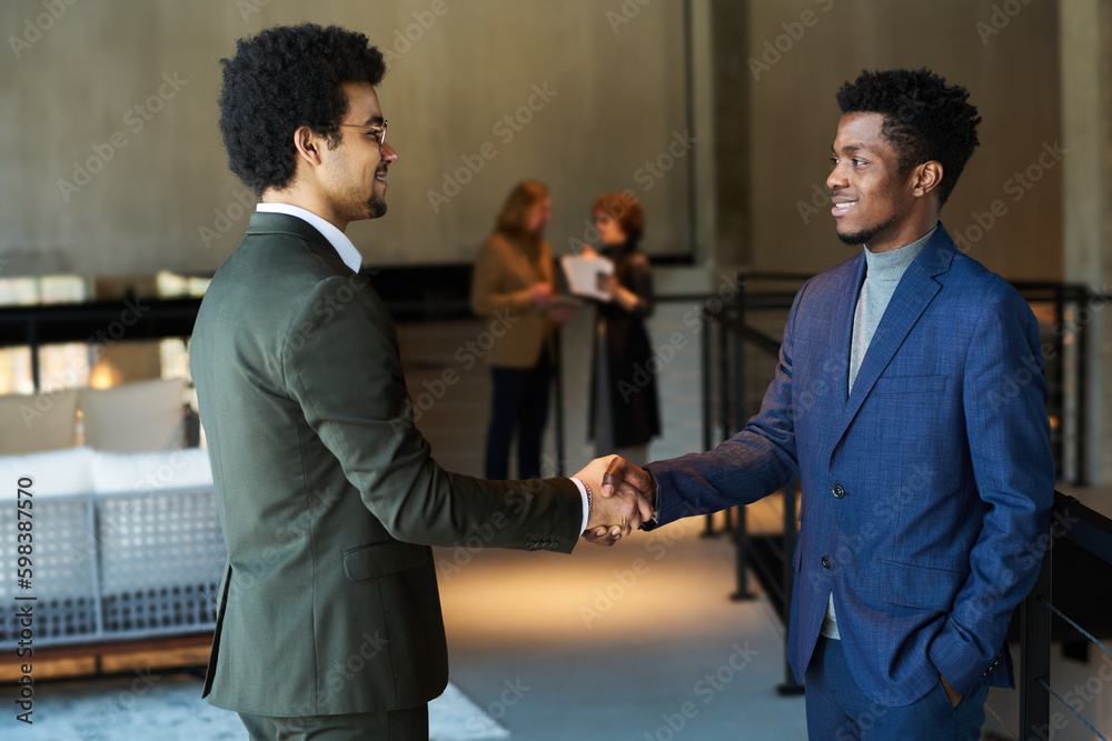 Aufkleber side view of two young male business partners shaking hands at meeting or while greeting one another
