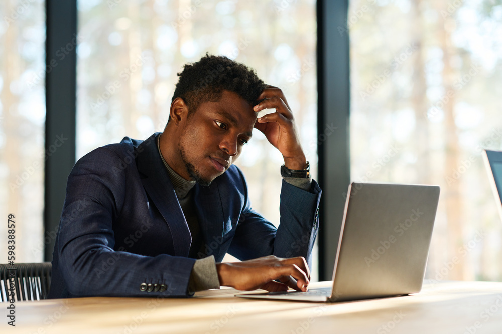 Aufkleber young pensive or tense businessman sitting by workplace in front of laptop in office and looking at 