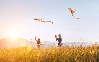 Smiling father with daughter as they releasing colorful kites on the high grass meadow. Warm family Summer outdoor photo moments or outdoor time spending concept image.