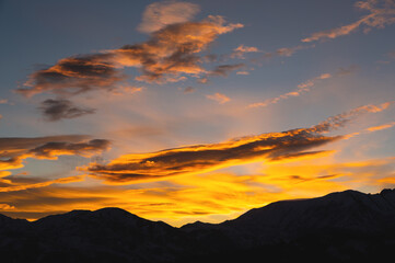 Colorful sunset over mountain hills. The black silhouette of the mountains is visible through the picturesque glow