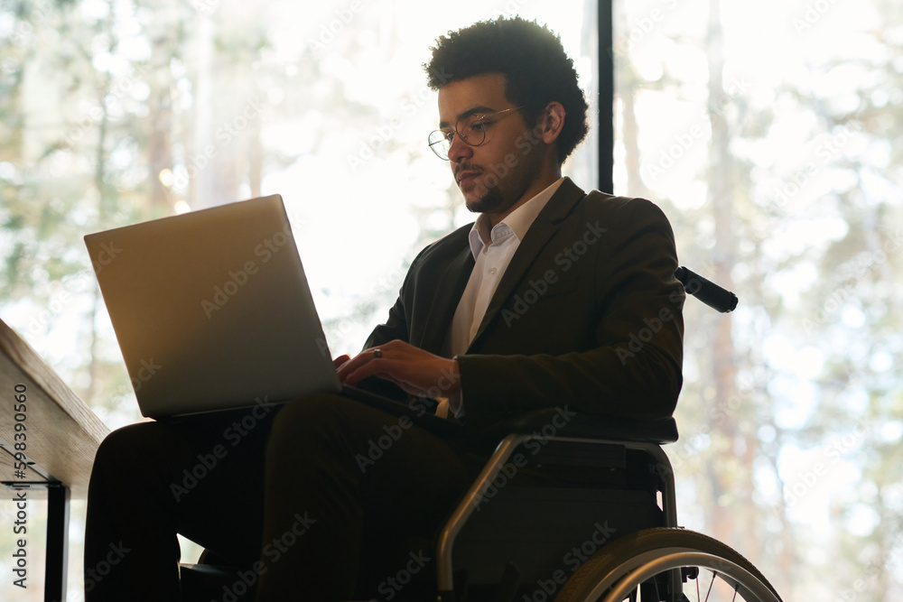 Aufkleber young multi-ethnic businessman with disability using laptop while sitting in wheelchair in front of 
