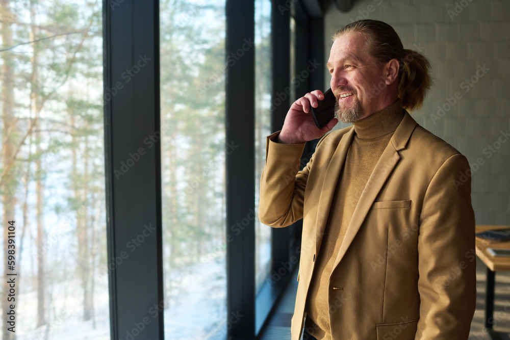 Poster smiling chief executive officer in formalwear looking through large office window while standing in 
