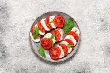 Caprese salad. Italian salad with chopped tomatoes, mozzarella, basil, olive oil on a light stone background. Top view, flat lay