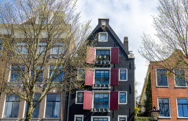 Historic old warehouse now turned into a home along a canal in Amsterdam with red shutters