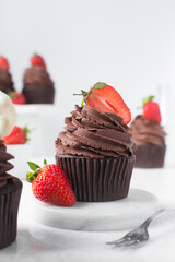Chocolate cupcake with dark chocolate buttercream and strawberries, double chocolate cupcakes with american buttercream, tall swirl frosting on a cupcake with a strawberry