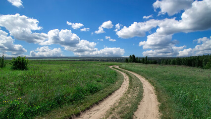 Green meadow with road under blue sky with clouds