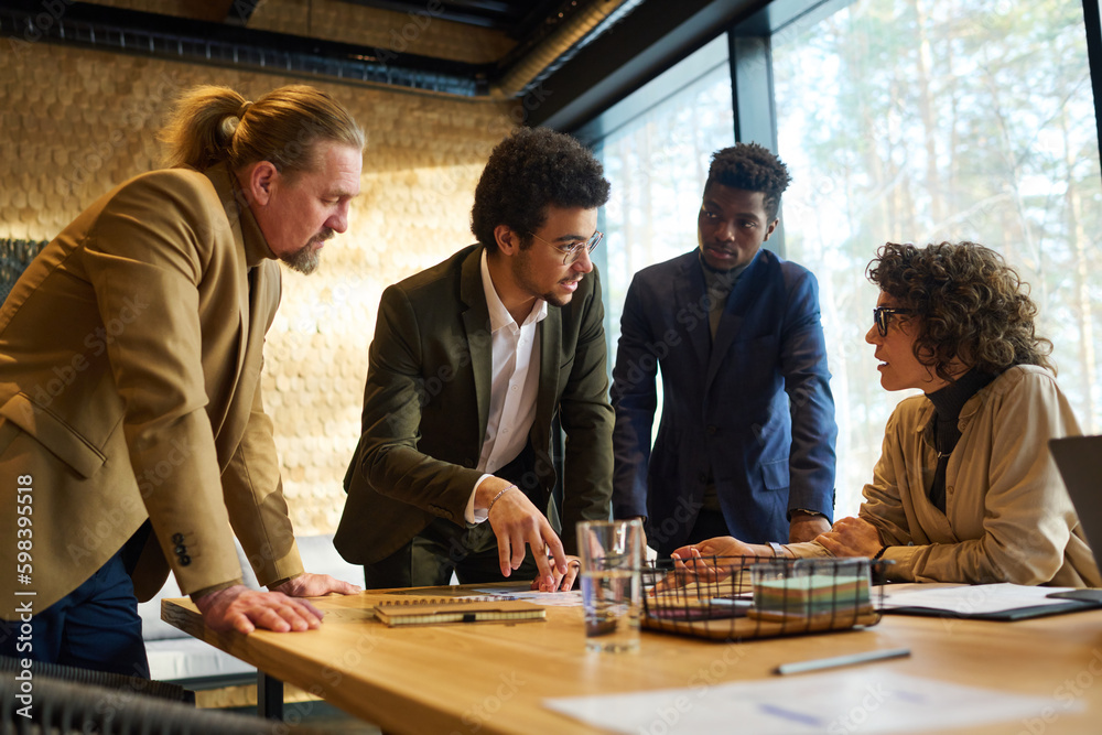 Poster Confident multi-ethnic businessman explaining data to intercultural colleagues while pointing at document during discussion