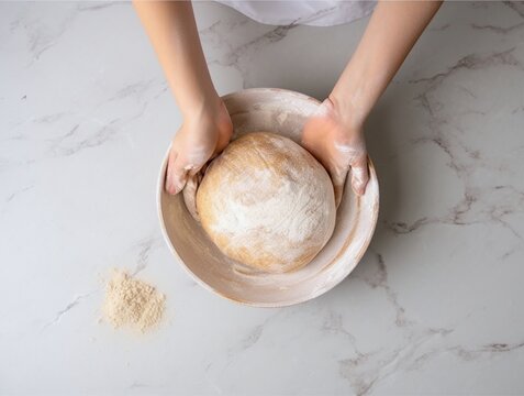 Woman's hands kneading bread dough in a bowl on white marble background