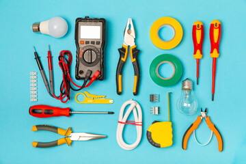 Electrician equipment on blue background with copy space.Top view.Electrician tool set.Multimeter, tester,screwdrivers,cutters,duct tape,lamps,tape measure and wires.Flet lay. © Avocado_studio