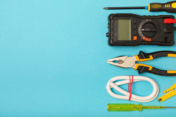 Electrician equipment on blue background with copy space.Top view.Electrician tool set.Multimeter, tester,screwdrivers,cutters,duct tape,lamps,tape measure and wires.Flet lay. © Avocado_studio