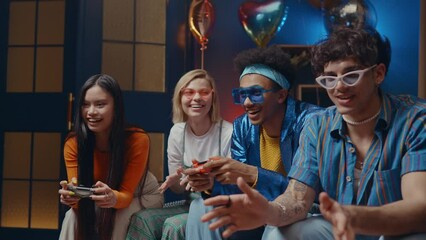 Group of friends making party at home and playing video games in the living room. Multiethnic group of young people having fun at home. Concept about technology and lifestyle