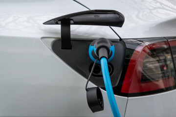 Ein weißes Elektro Auto hängt an der Ladesäule - Strom tanken mit Stecker in der Tanköffnung...