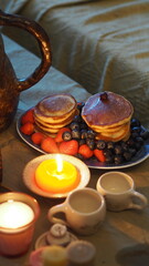 Fototapeta na wymiar Pancakes with berries, tea. Candles. Warm light.