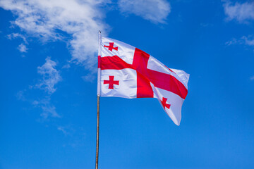 The flague of Georgia waving on bright blue sky background. 
