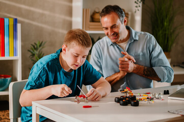 Blond young boy assembling his toy patiently while his dad is watching with joy.