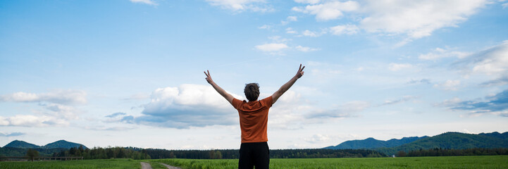 View from behind of a young man with his arms raised in victorious gesture