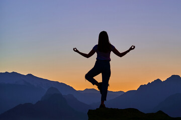 Back of silhouette of girl during meditation training on the top of a mountain hill at sunset. Calm...