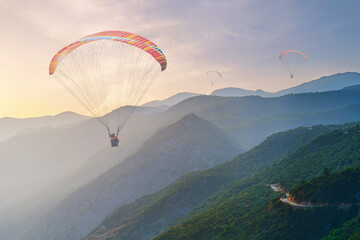 Landscape of flying paraglider over idyllic mountains with haze at sunset with soft light