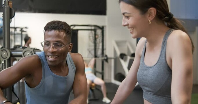 Cheerful woman and black trainer talking in gym