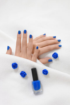 Blue manicure. Close up of woman hands with blue nails on white blanket. Her hands are partially covered by white coverlet. Beauty concept.