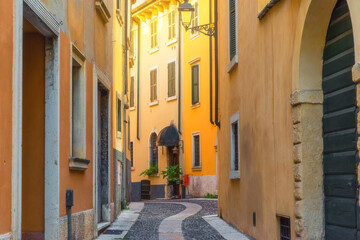 Fototapeta na wymiar Medieval narrow paving stone street with yellowl buildings in Verona town, Veneto, Italy, Empty Italian street in old town