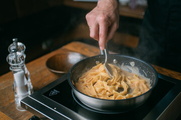 The male hands of the chef prepare a classic homemade pasta in a frying pan. Close-up.