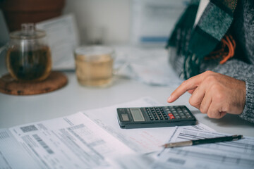 Close-up of a man's hands with a calculator and a lot of utility bills on the table. The man considers the costs of gas, electricity, heating.