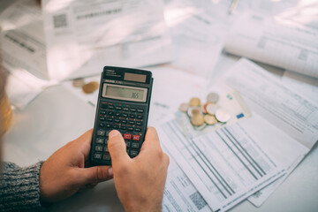 Close-up of a man's hands with a calculator and a lot of utility bills, some coins on the table.