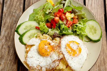 Fried eggs with fresh salad and potato mash outdoors on wood table